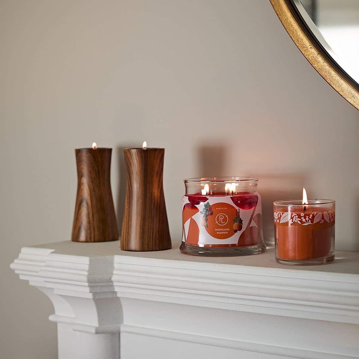 Woodland Pumpkin Mini Jar Candle lit shown with a 3-Jar Candle also lit on a wooden Tealight holder pair on a white mantle piece.