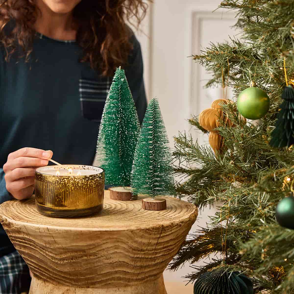 Whiskey & Oak 3-Wick Ripple Jar Candle being lit by a lady with a long match stick on a wooden surface with a Christmas theme background.