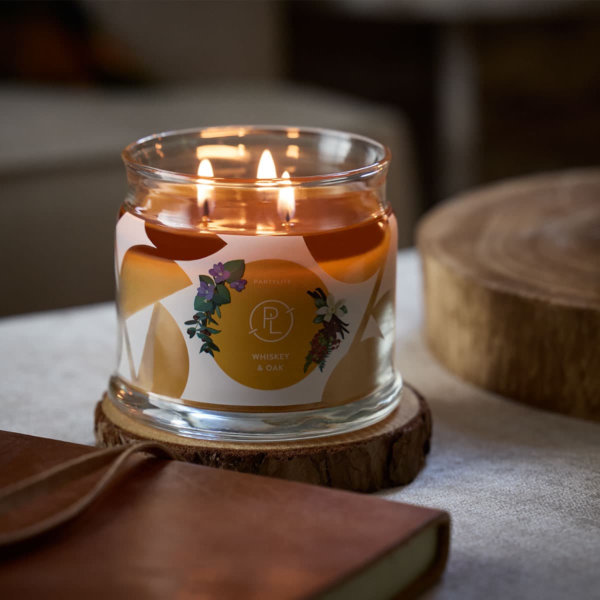 Whiskey & Oak 3-wick Jar Candle lit on a round wooden coaster with a blurred background.