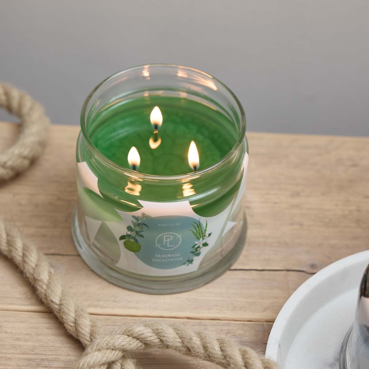 Seagrass Eucalyptus 3-Wick Jar Candle on a wooden surface with a rope lying next to it.