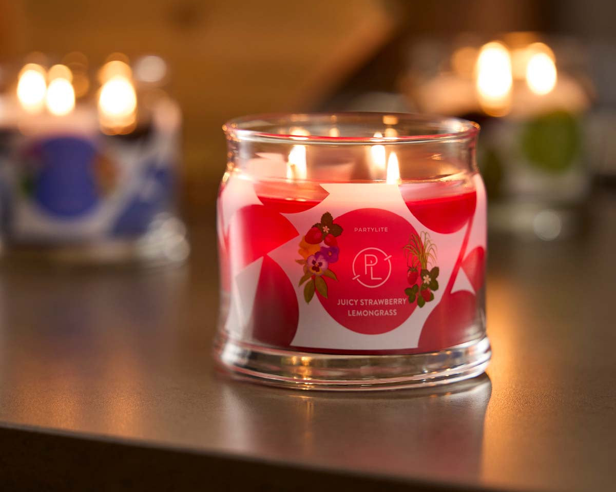 Juicy Strawberry Lemongrass 3-wick Jar Candle lit on a wooden surface.