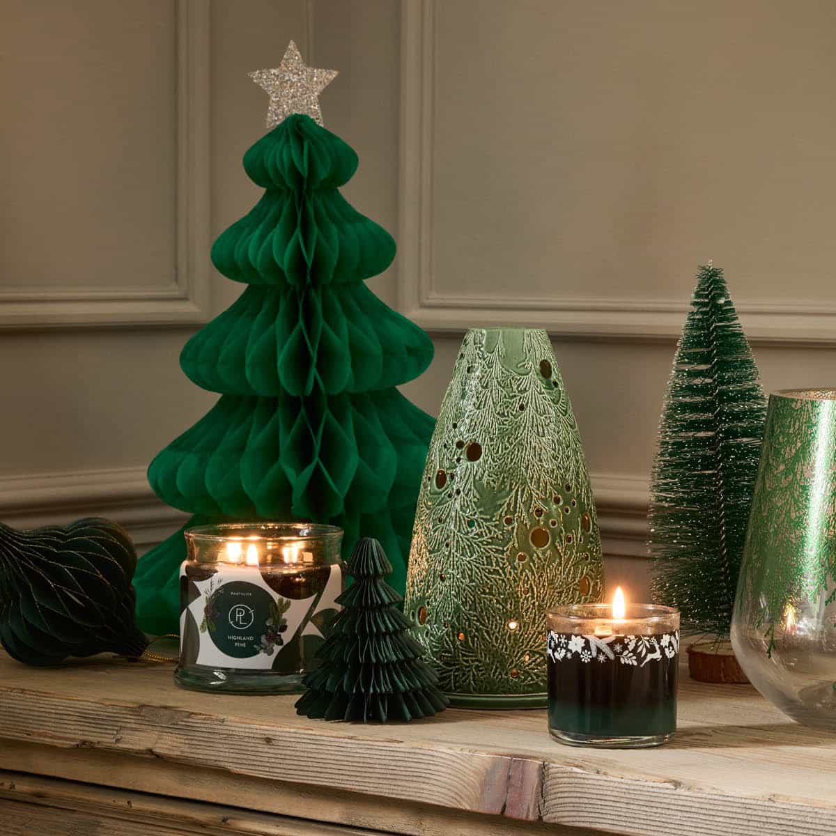 Highland Pine Mini Jar Candle, shown with the 3-wick Jar Candle both lit with the Lacy Green Tealight holder and Christmas themed items on a wooden surface.