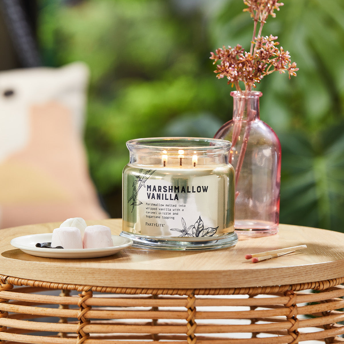 Marshmallow Vanilla 3-wick jar shown on a wooden tray with a  clear pink bottle of flowers next to it and two unlit long match sticks